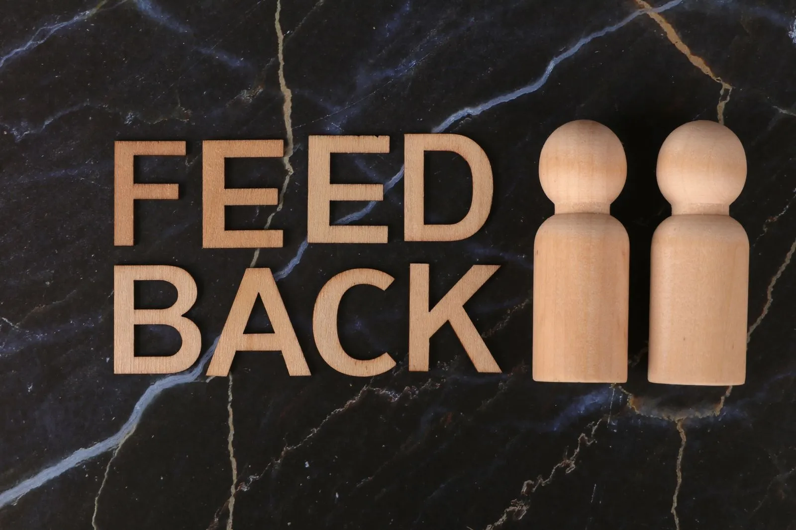 Schriftzug „Feedback“ mit zwei Holzfiguren