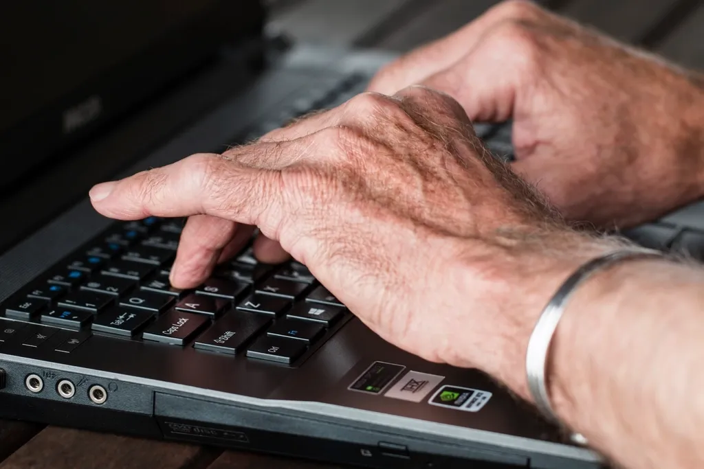 Hände eines älteren Menschen tippen auf einer Laptop-Tastatur